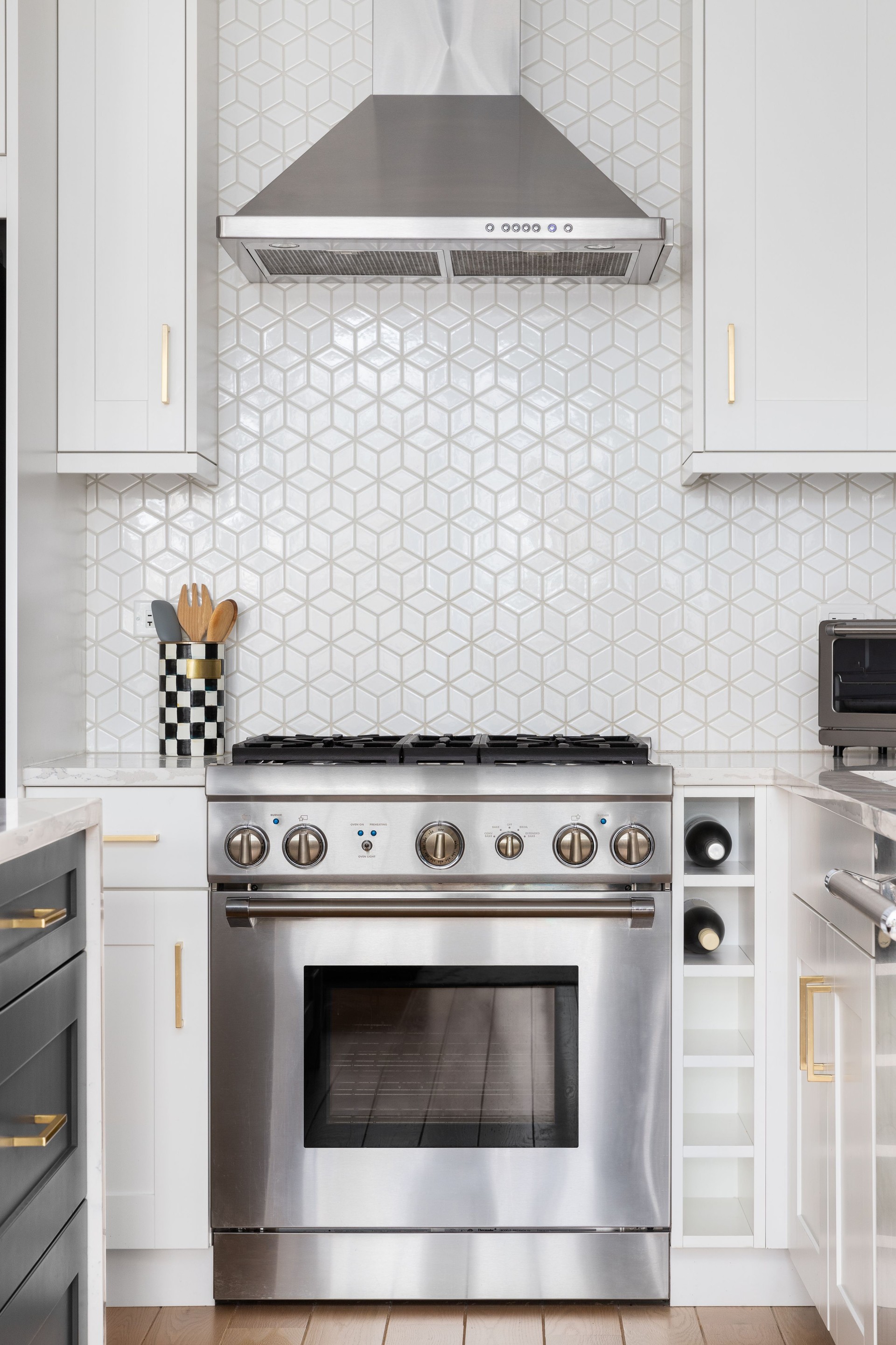 A stove detail with white cabinets and a tiled backsplash.