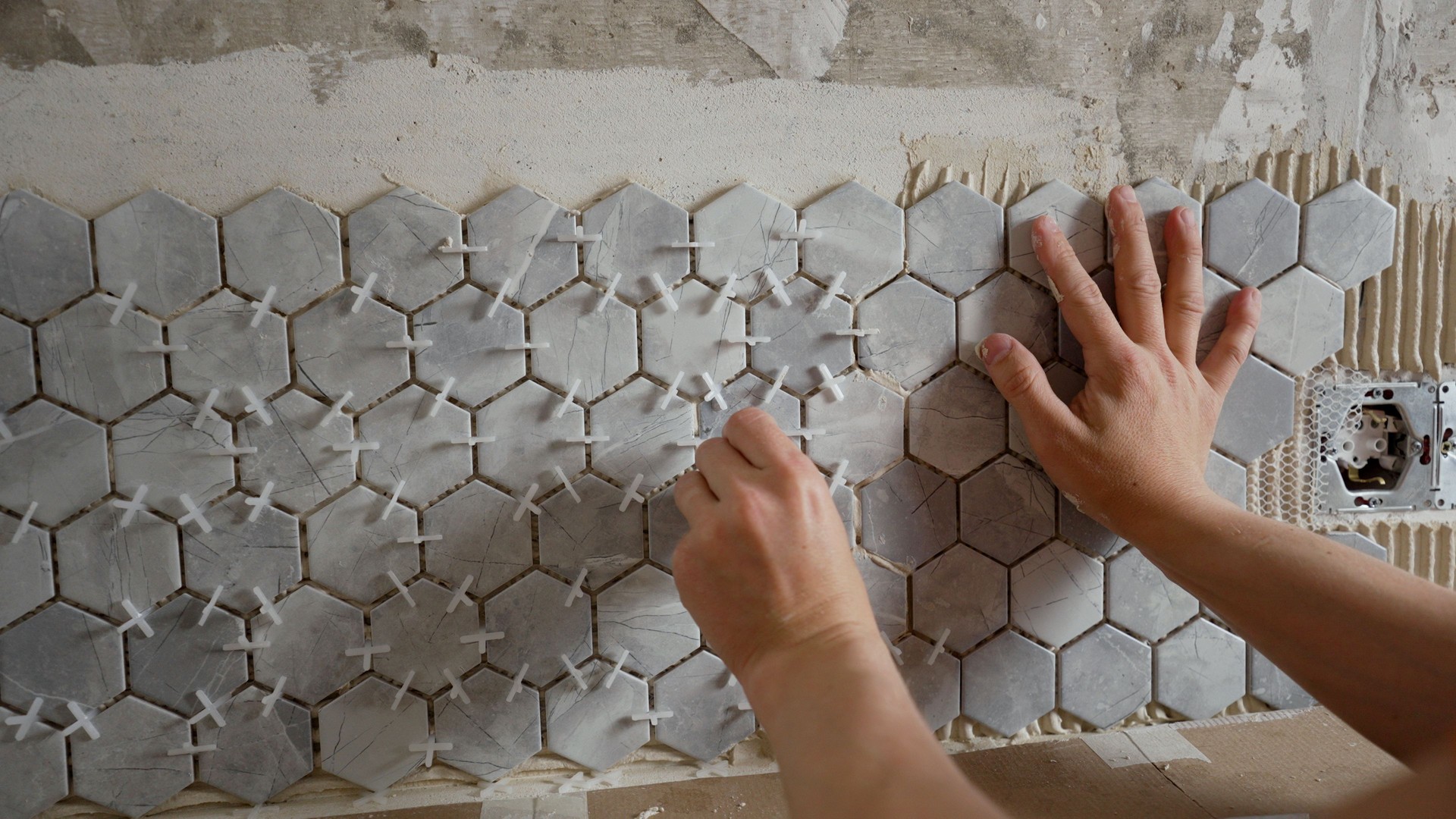 Construction worker placing hexagonal tiles on wall during renovation